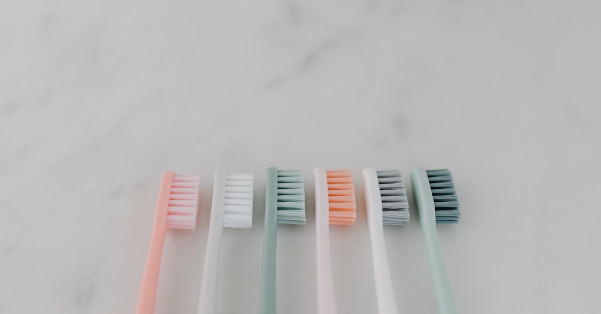 Six pastel-colored toothbrushes arranged side by side on a light gray surface.